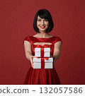 happy woman in a red dress holding two gifts without a santa hat on a red studio background 132057586