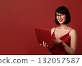 smiling lady in glasses, red dress working on red laptop on red background 132057587