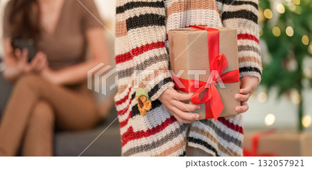 Christmas Gift Exchange. Child presenting a wrapped present to a joyful woman in festive attire. Christmas Gift Exchange. Child presenting a wrapped present to a joyful woman in festive attire. 132057921