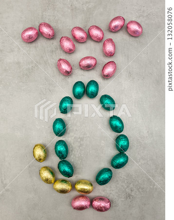 Chocolate easter eggs forming a rabbit shape on a textured surface 132058076