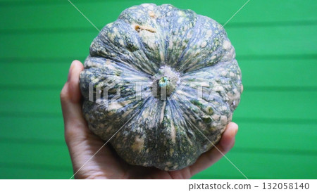 Hand Holding a Small Pumpkin Against a Green Background 132058140