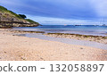 Sunny Beach With Calm Sea, Boats Off Shore, Rocky Cliff, And Seagrass Along The Shoreline 132058897