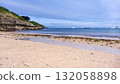 Sunny Beach With Calm Sea, Boats Off Shore, Rocky Cliff, And Seagrass Along The Shoreline 132058898