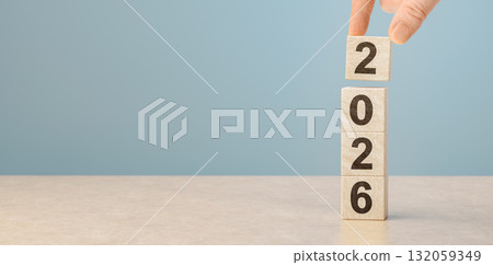 Hand building 2026 new year concept with wooden blocks. Male hand placing number two on stack of wood cubes 132059349