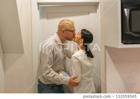 Couple Kissing Kitchen Doorway Romance: Affectionate couple embraces passionately near kitchen doorway, showcasing intimate moment; likely a romantic scene. 132059565