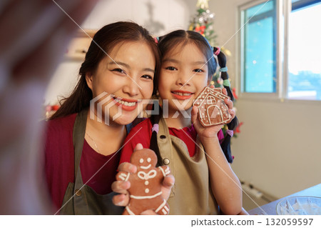 Holiday Treats. Mother and daughter proudly displaying their decorated gingerbread cookies. 132059597