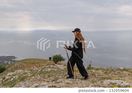 A woman is walking on a hill with a stick and a hat on 132059604