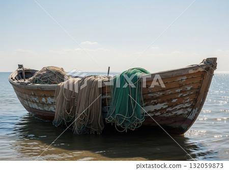 Quiet wooden fishing vessel anchored close to shore with aged structure, folded nets, and shimmering reflections in calm coastal water under open sky 132059873