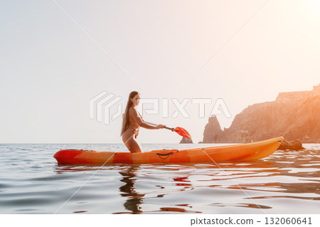 Kayaking, Woman, Ocean: A woman paddling a kayak in a calm ocean with a rocky coastline in the background. Kayaking, Woman, Ocean: A woman paddling a kayak in a calm ocean with a rocky coastline in the background. 132060641