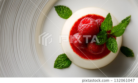 Panna Cotta with Raspberry Sauce, Fresh Berries, and Mint on Textured White Plate 132061047