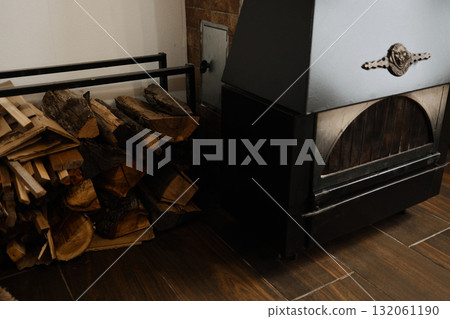 Black metal fireplace with stacked firewood and brick-patterned wall in a cozy home interior. Perfect for design, lifestyle, or winter comfort themes 132061190
