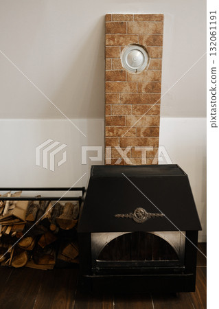 Black metal fireplace with stacked firewood and brick-patterned wall in a cozy home interior. Perfect for design, lifestyle, or winter comfort themes 132061191