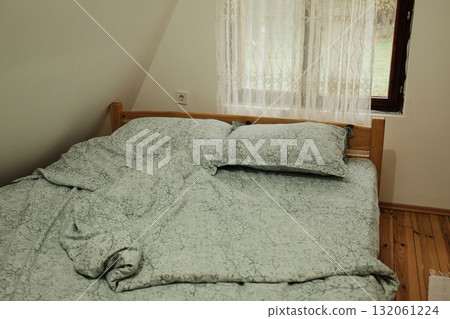 Rustic bedroom interior with a wooden bed, crumpled blanket, and lace curtain letting in daylight. Perfect for lifestyle, home, or interior design concepts Rustic bedroom interior with a wooden bed, crumpled blanket, and lace curtain letting in daylight. Perfect for lifestyle, home, or interior design concepts 132061224