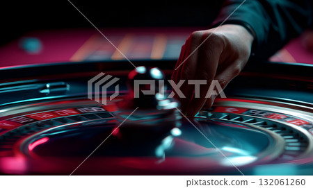 Roulette Wheel in Casino with Hand Placing Ball Under Dramatic Red and Blue Lighting 132061260