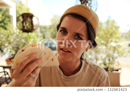 Young woman in yellow beanie holding a taco and looking at camera in Mexican cafe Young woman in yellow beanie holding a taco and looking at camera in Mexican cafe 132061423