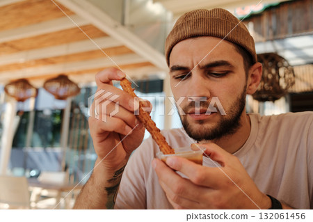Man dipping fried churro stick into sauce while sitting in Mexican cafe Man dipping fried churro stick into sauce while sitting in Mexican cafe 132061456