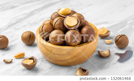 Macadamia nuts with shell in wood bowl with cracked macadamia  and tool on marble table Macadamia nuts with shell in wood bowl with cracked macadamia  and tool on marble table 132061468