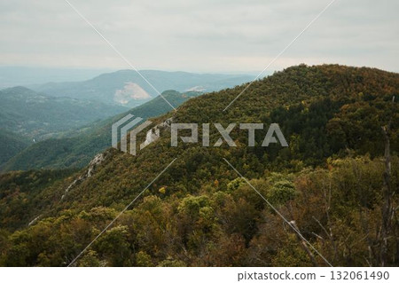 Wide view of forested mountain ridges with colorful autumn foliage and distant hills under cloudy sky. View from Kablar mount Wide view of forested mountain ridges with colorful autumn foliage and distant hills under cloudy sky. View from Kablar mount 132061490