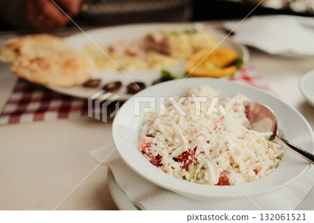 Traditional Balkan shopska salad made of tomato, cucumber, and grated cheese served in a white bowl on restaurant table Traditional Balkan shopska salad made of tomato, cucumber, and grated cheese served in a white bowl on restaurant table 132061521