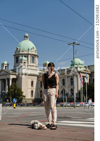 Woman with red merle Border Collie puppy standing in front of the Serbian Parliament building in Belgrade. Travel with pet concept. 132061662