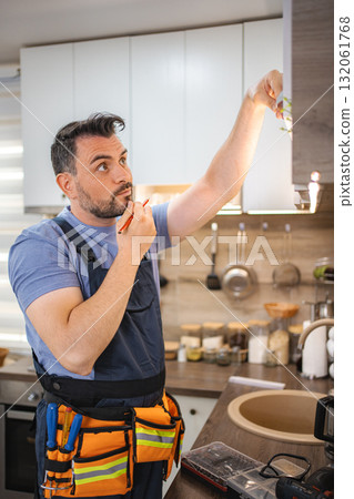 Handyman repairing kitchen cabinets and thinking about next steps 132061768