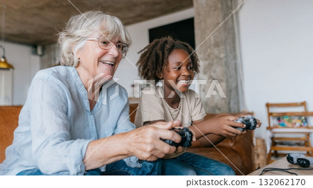 White grandmother and black granddaughter joyfully playing video games together, showcasing multigenerational bonding and emotional connection in family life 132062170