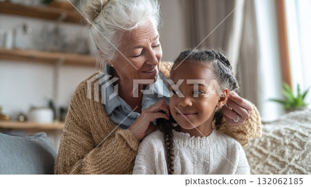 Grandmother lovingly braiding granddaughter's hair in cozy living room, showcasing multigenerational family life and emotional connection Grandmother lovingly braiding granddaughter's hair in cozy living room, showcasing multigenerational family life and emotional connection 132062185