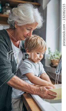 Grandmother and toddler joyfully washing dishes together in a cozy kitchen, showcasing multigenerational family life and emotional connection Grandmother and toddler joyfully washing dishes together in a cozy kitchen, showcasing multigenerational family life and emotional connection 132062215