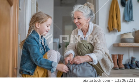 Grandmother and granddaughter joyfully organizing backpack together in a cozy home environment, showcasing multigenerational family connection and love 132062221