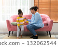 Mother and daughter playing together in living room while sitting on pink couch 132062544