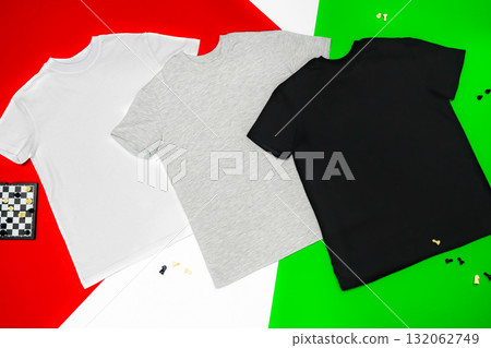 Close-up of the three t-shirts (black, white and grey) on color background redand green. 132062749