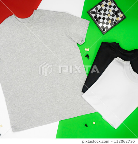 Close-up of the three t-shirts (black, white and grey) on color background redand green. Close-up of the three t-shirts (black, white and grey) on color background redand green. 132062750