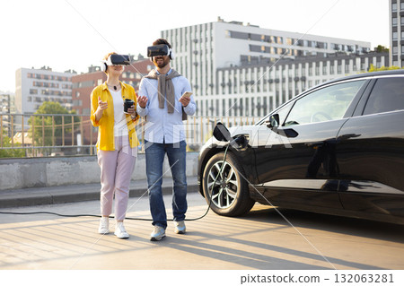 A couple wearing VR headsets while their electric vehicle charges in an urban setting. A couple wearing VR headsets while their electric vehicle charges in an urban setting. 132063281