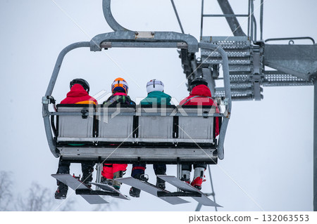Four female snowboarders on chairlift climb mountain Four female snowboarders on chairlift climb mountain 132063553