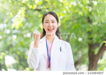 Woman in white coat outdoors, fresh greenery, fist pump Woman in white coat outdoors, fresh greenery, fist pump 132064897