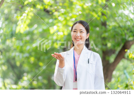 Woman in white coat outdoors, fresh greenery, hand-waving Woman in white coat outdoors, fresh greenery, hand-waving 132064911