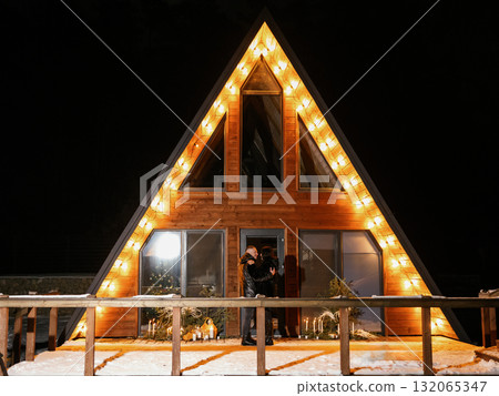 Couple hugging in front of illuminated chalet at night Couple hugging in front of illuminated chalet at night 132065347