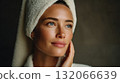 Woman with towel wrapped around her head gazes thoughtfully, showcasing clear skin and serene expression 132066639