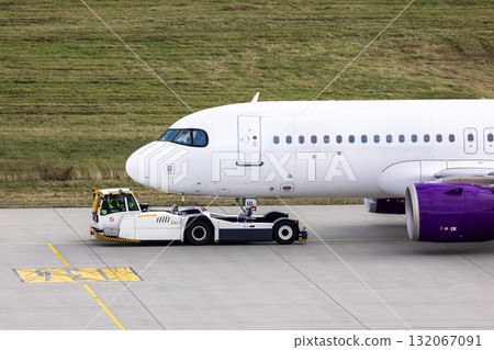 Modern regional jet aircraft towed by ground vehicle on airport taxiway tarmac under sunlight. Engine cockpit clearly visible crew performs technical operations before next scheduled flight airport Modern regional jet aircraft towed by ground vehicle on airport taxiway tarmac under sunlight. Engine cockpit clearly visible crew performs technical operations before next scheduled flight airport 132067091
