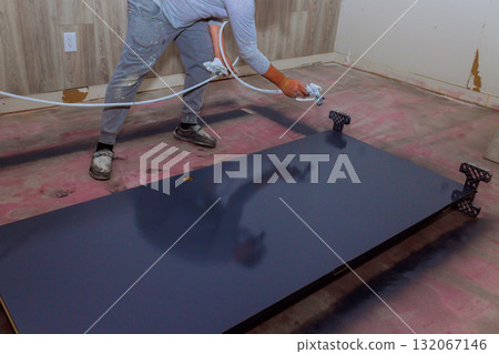 Painter applies smooth coat of navy paint to large tabletop, revealing fresh look in renovated room. 132067146