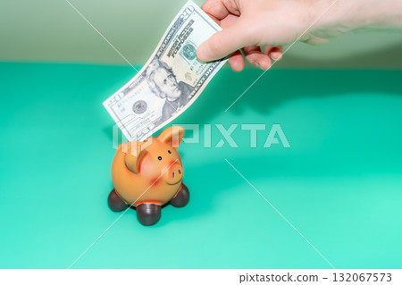A hand deposits a twenty-dollar bill into a piggy bank, symbolizing saving and financial planning, amidst the backdrop of an economic crisis. A hand deposits a twenty-dollar bill into a piggy bank, symbolizing saving and financial planning, amidst the backdrop of an economic crisis. 132067573