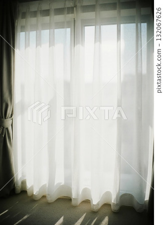 Sheer grey curtains gently sway as bright sunlight streams through a large window, creating a warm and inviting atmosphere in the room during morning hours Generative AI 132067626