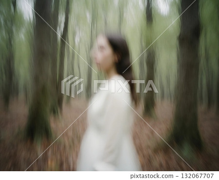 In a dense, fog-filled forest, a spectral woman wearing a flowing white dress stands among towering trees. The eerie atmosphere captures the sense of an otherworldly presence at dusk Generative AI 132067707