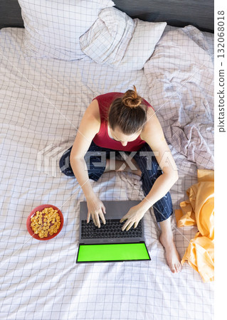 Enjoying Black Friday Shopping in Bed With Laptop and Snacks for a Cozy Experience 132068018