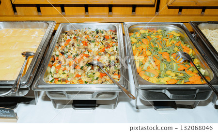 A vibrant buffet setup featuring assorted trays filled with colorful cooked vegetables. Perfect for catering events, showcasing healthy vegetarian options and variety in food presentation A vibrant buffet setup featuring assorted trays filled with colorful cooked vegetables. Perfect for catering events, showcasing healthy vegetarian options and variety in food presentation 132068046