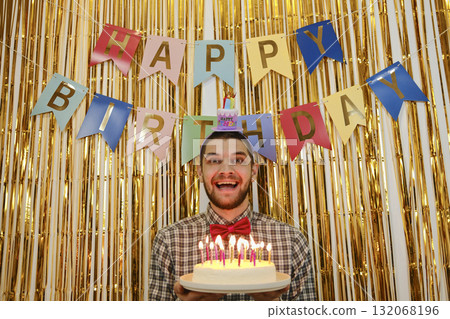 Smiling man with birthday cake and candles, party banner and golden festive backdrop 132068196