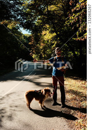 Smiling man with map hitchhiking on a road in forest with his Australian Shepherd dog. Travel with dog concept Smiling man with map hitchhiking on a road in forest with his Australian Shepherd dog. Travel with dog concept 132068267