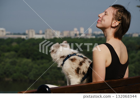 Smiling young woman with her red merle border collie puppy sitting on a bench in Kalemegdan Fortress, Belgrade, with city view in background Smiling young woman with her red merle border collie puppy sitting on a bench in Kalemegdan Fortress, Belgrade, with city view in background 132068344