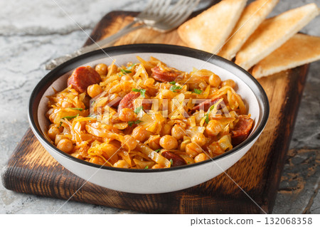 Spanish traditional cabbage, chickpea stew with paprika and sausages close-up in a plate. Horizontal Spanish traditional cabbage, chickpea stew with paprika and sausages close-up in a plate. Horizontal 132068358