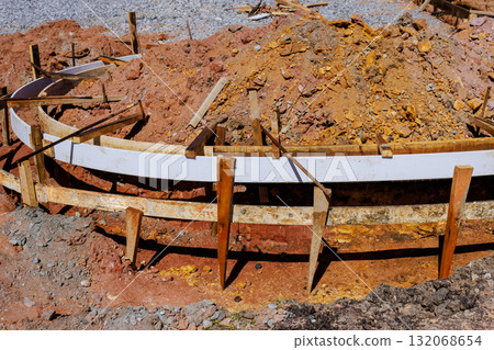 Wooden forms for concrete are set for sidewalk curb in construction site, surrounded by dirt gravel Wooden forms for concrete are set for sidewalk curb in construction site, surrounded by dirt gravel 132068654